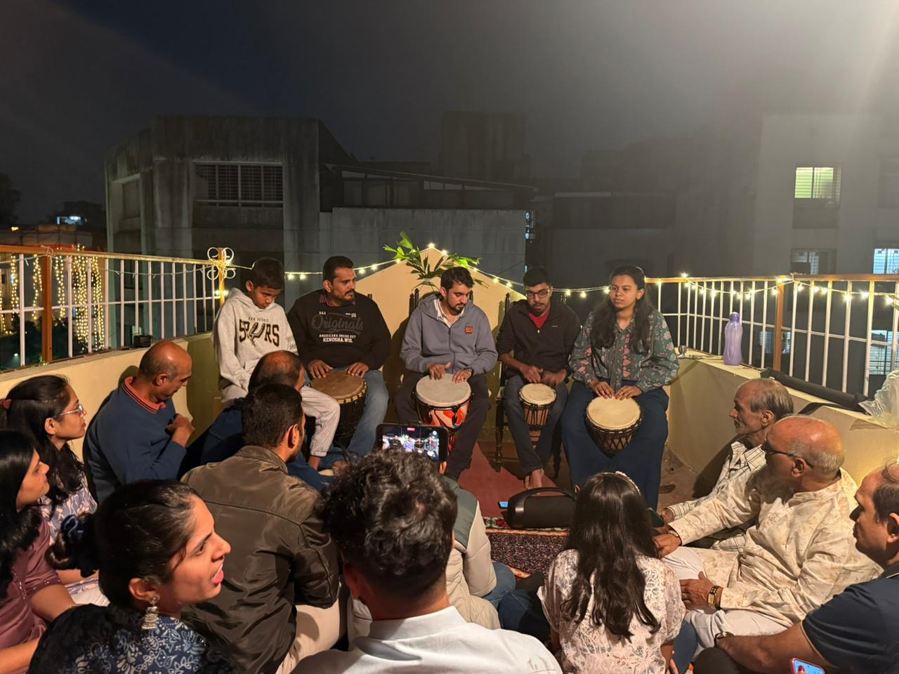Live music concert at home with jembe and cajon players performing on a rooftop with family audience.