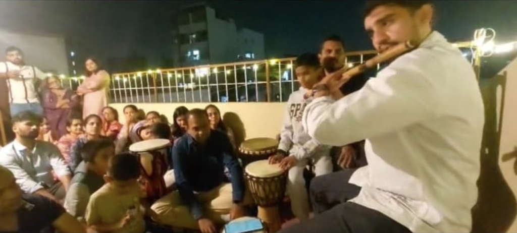 Live flute performance with jembe percussion during a home music concert on a rooftop with family audience.