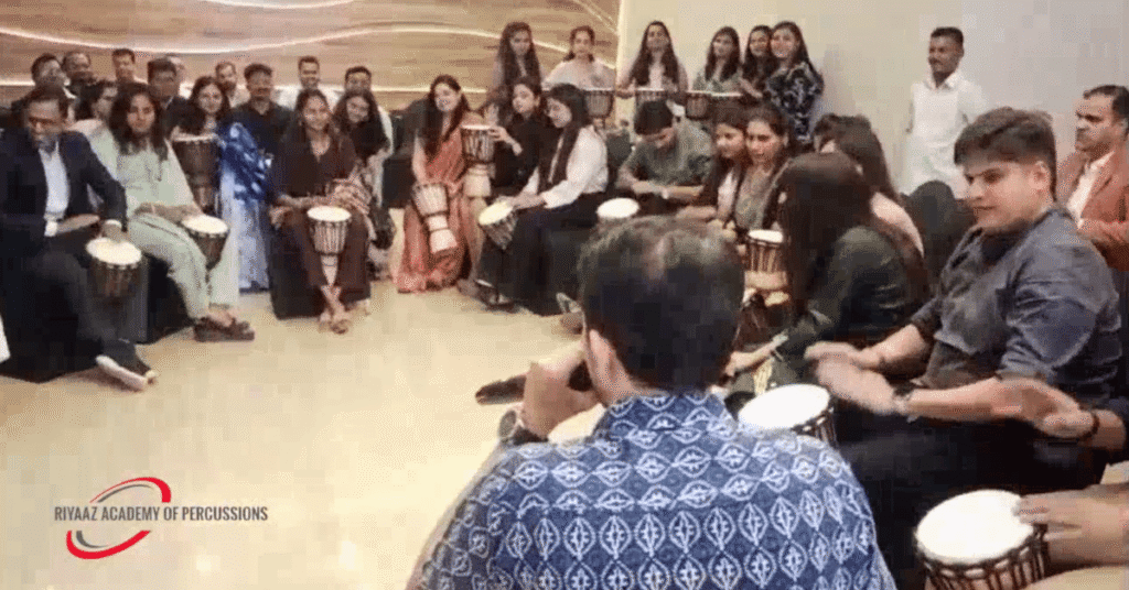 Corporate Team Building Activities in Pune: How Rhythm and Music Can Transform Workplace Teams 2 Corporate team building activity with employees participating in a Djembe drum circle led by Riyaaz Academy in Pune